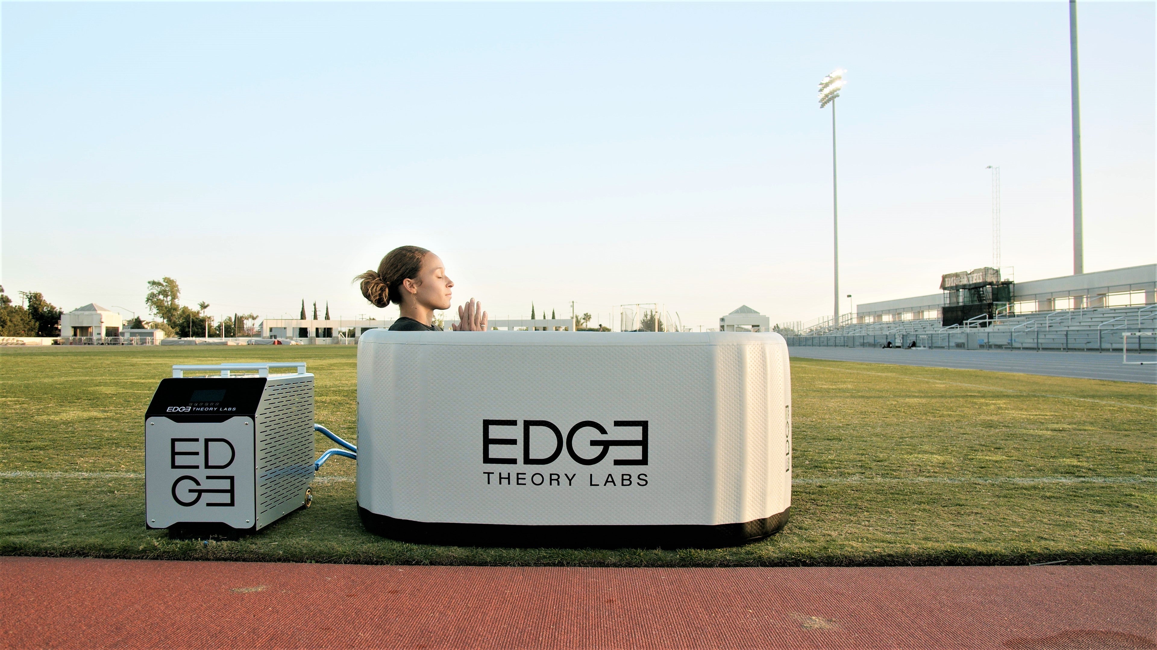 woman on a turf field taking a cold plunge in an edge tub with praying hands