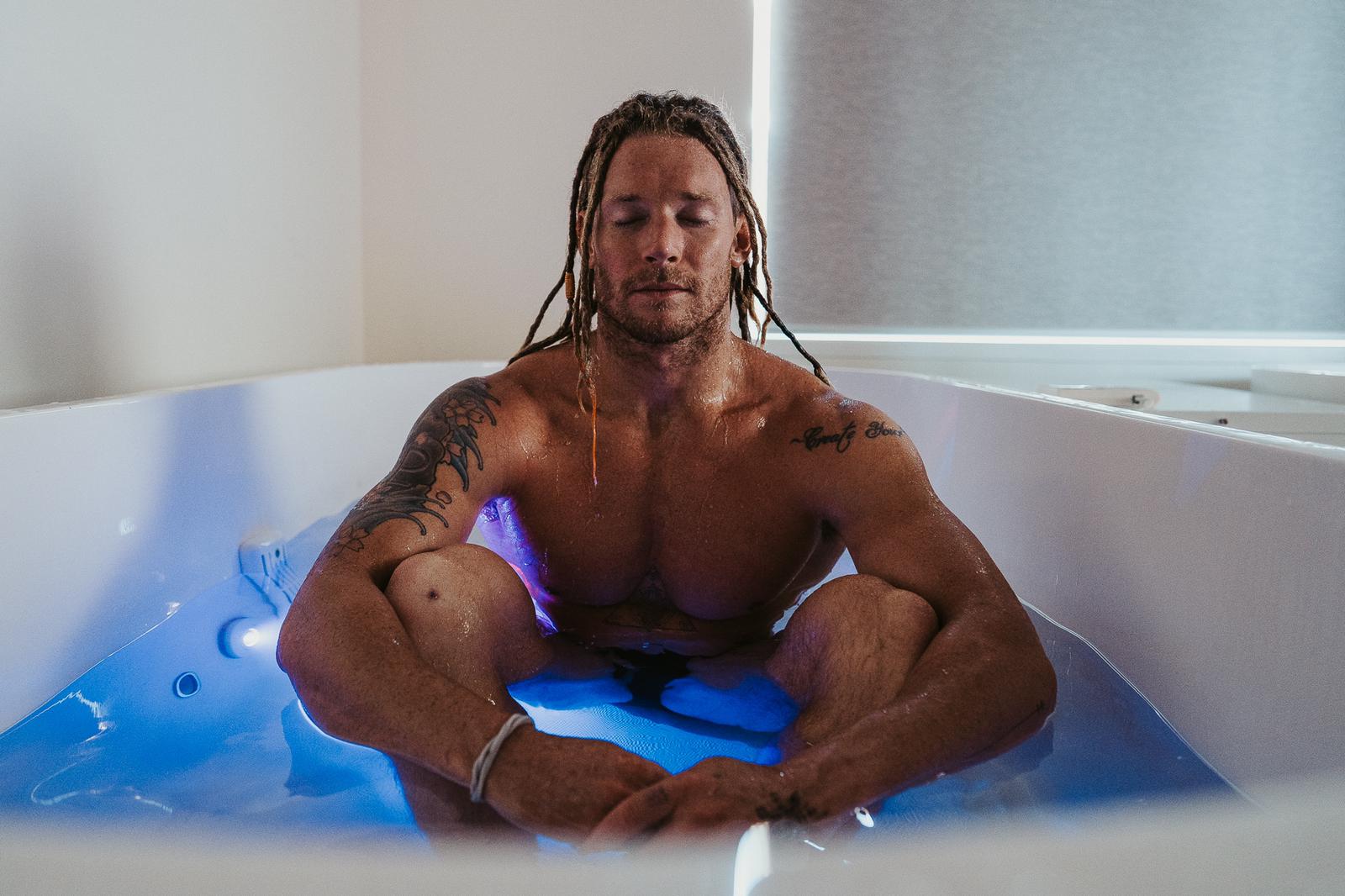man with eyes closed in a dream pod ice bath lit by led lights