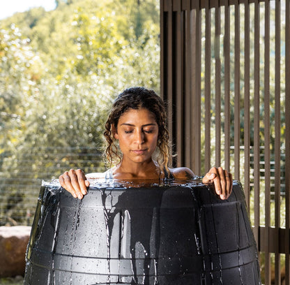 Calm woman in an Ice Barrel ice bath with trees in the background 